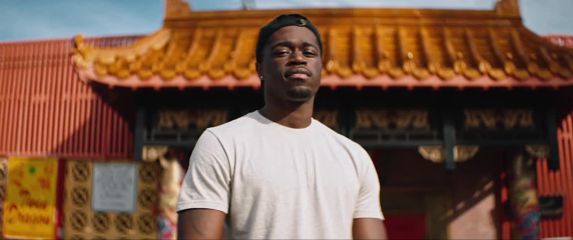 A black man looking into the camera while standing in front of a building in an east asian architectural style