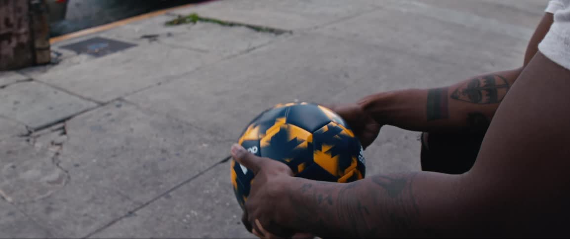 Man sitting on bench in front of painted mural passes soccer ball from hand to hand