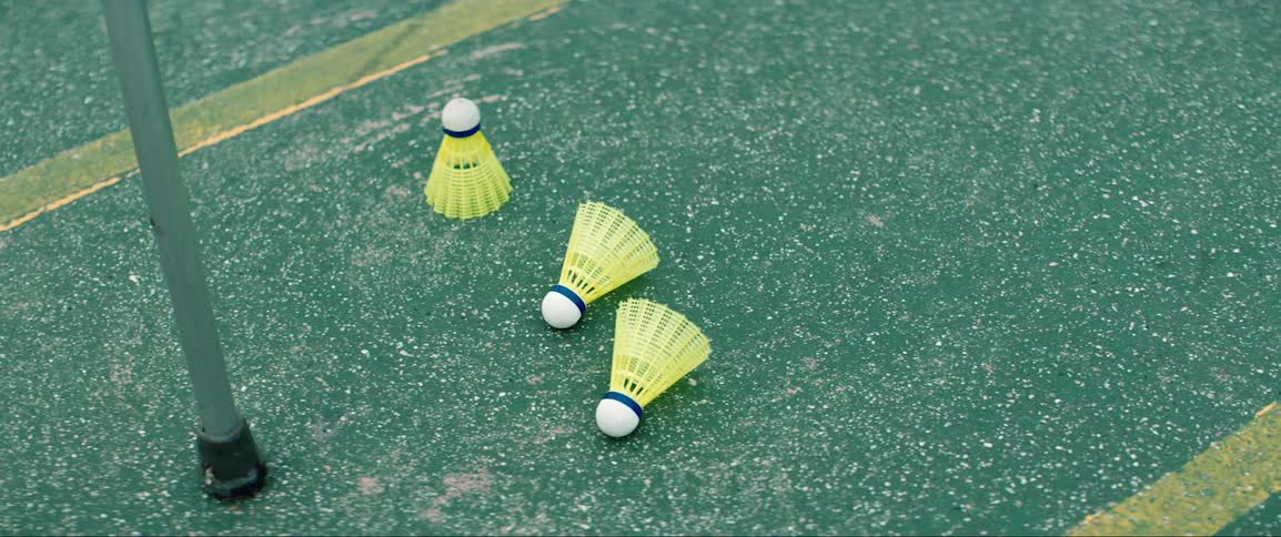 Three yellow shuttlecocks sit on a ground covered in green paint and yellow lines