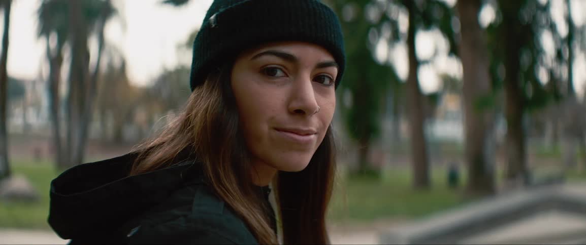 A woman sits in the park with her skateboard