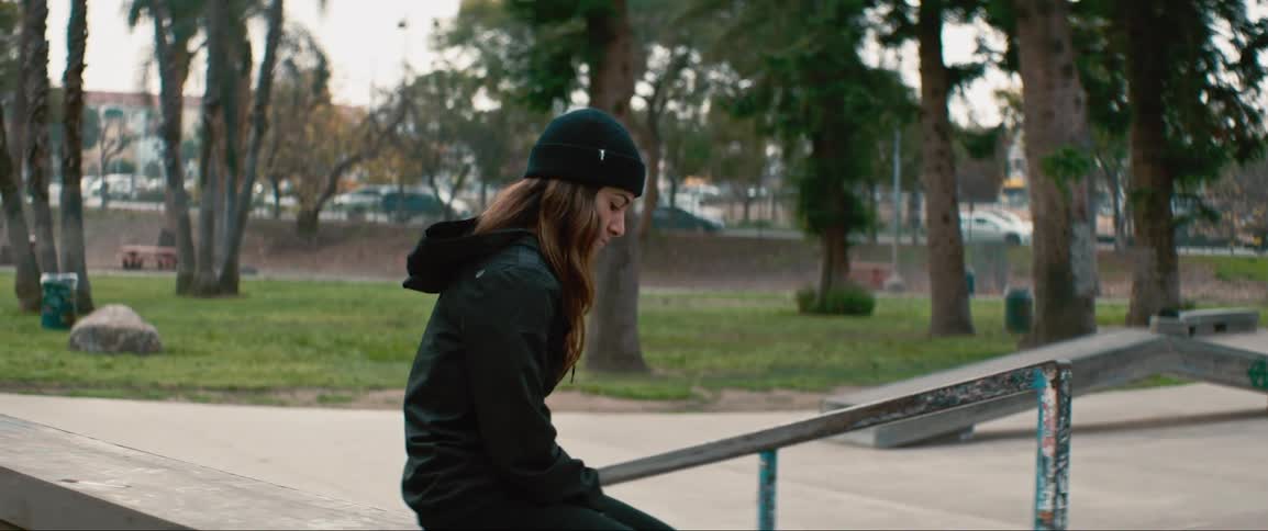 Young woman with skateboard sits on concrete wall in skate park