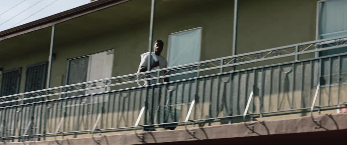 Man walks across balcony of apartment building carrying bag
