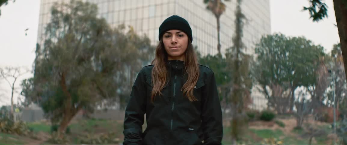 A girl poses with a skateboard in a city park