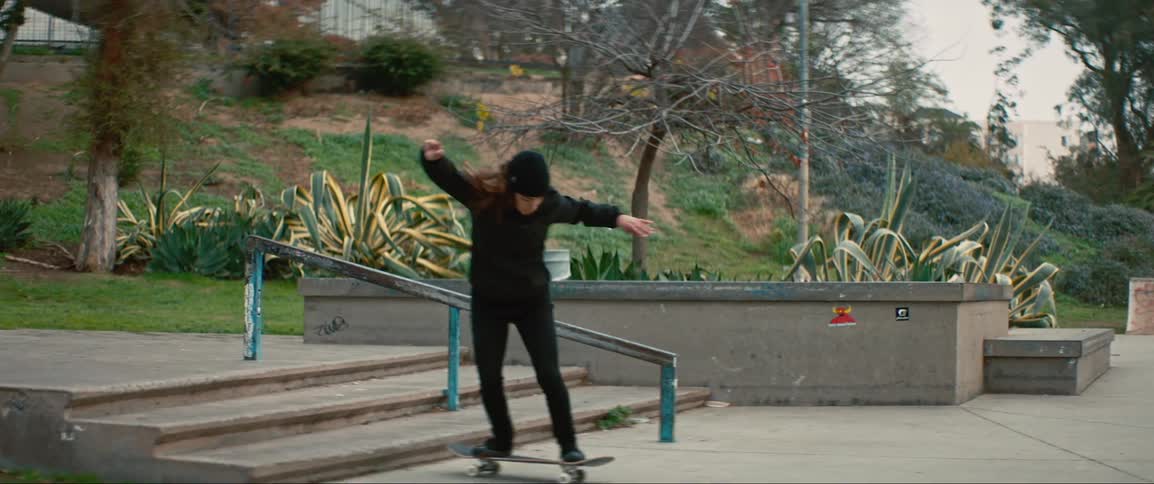A white girl jumps a staircase in a park on her skateboard