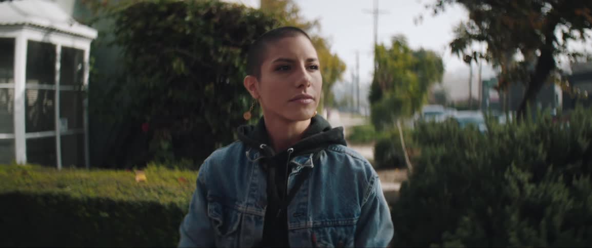 A hispanic woman with a shaved head walks down a neighborhood sidewalk