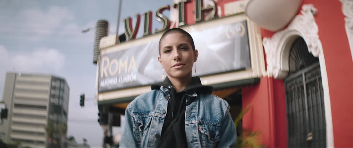 A short haired woman standing outside of a red building while grinning into the camera