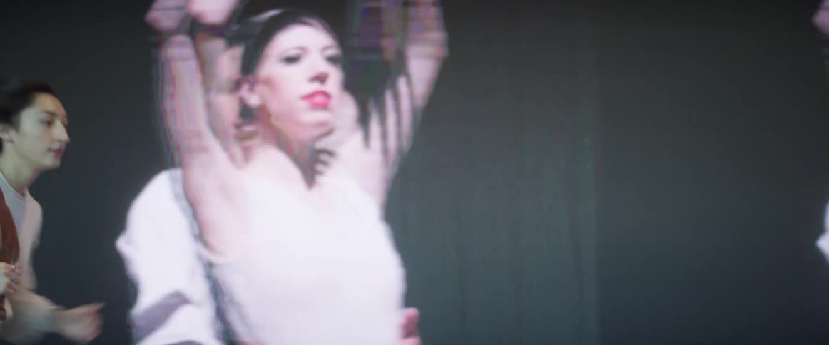 A woman checking her watch running down a hallway with large screens displaying a pair of dancers