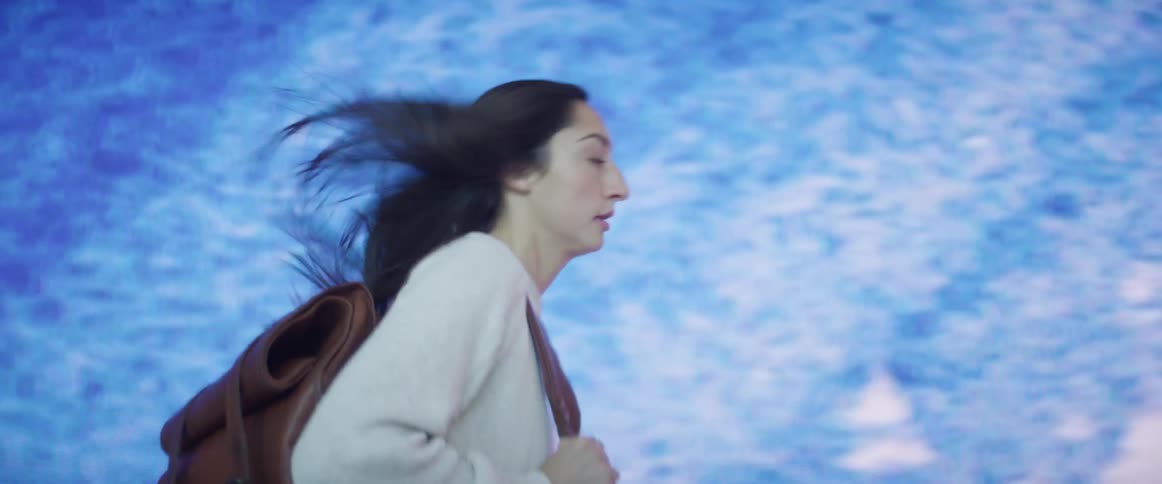 A young woman running pass a monitor that covers an entire wall while checking her watch