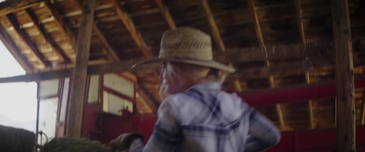 A woman lifts up a hay bale and moves it to another pile in a barn
