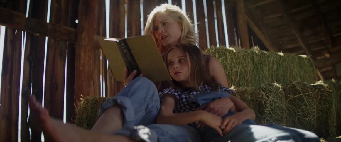 A woman and a girl sitting in a barn reading a book