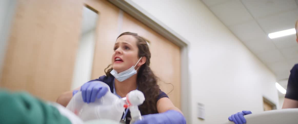 Doctors quickly pushing a stretcher with a patient on it down the hallway of a hospital while one pumps a cpr mask