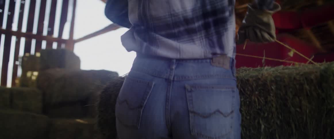 A female lifts and moves hay bales in a barn