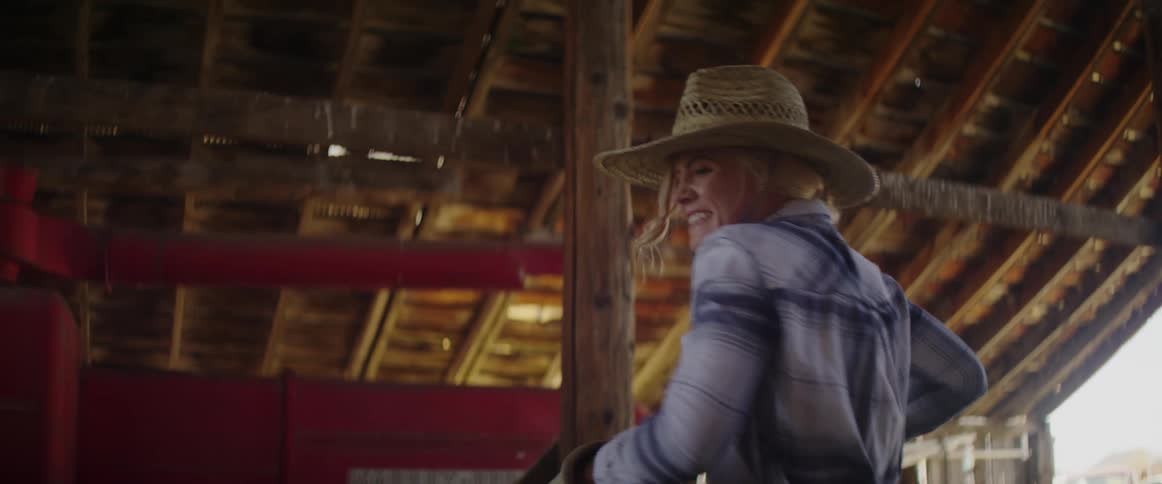 Female struggles as she picks up a bale of hay by the twine and moves it from one location in the barn to another