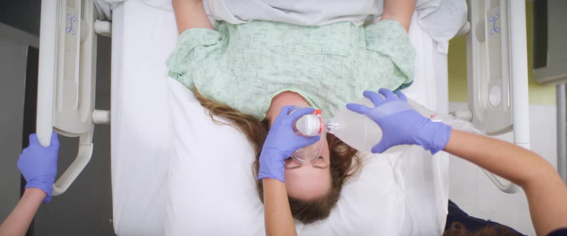 A nurse squeezes a breath bag on a female patient in a hospital