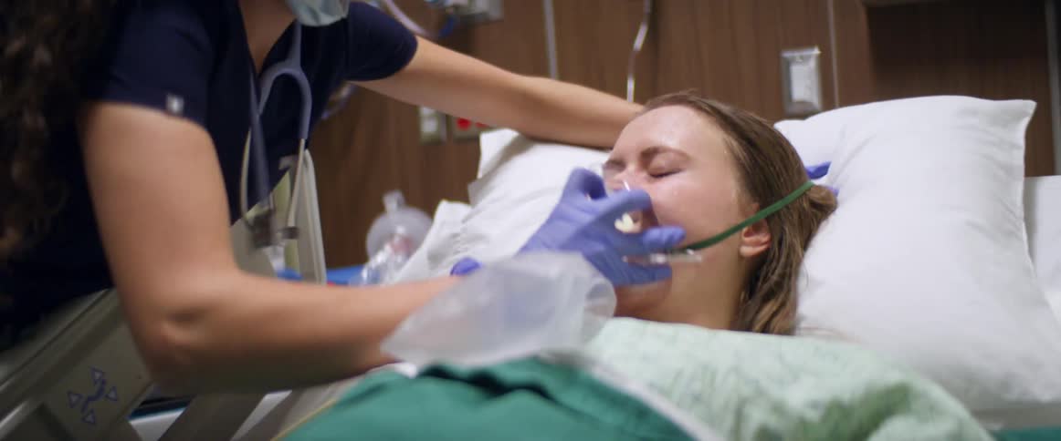 A nurse puts a breathing mask on a female patient in a hospital room
