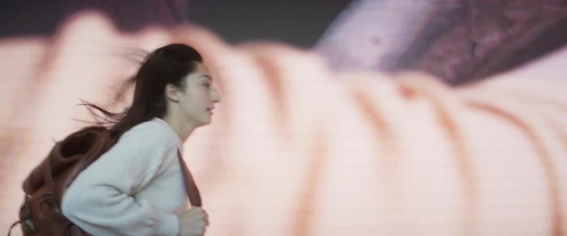 A college student runs through a theater and past a screen playing a movie