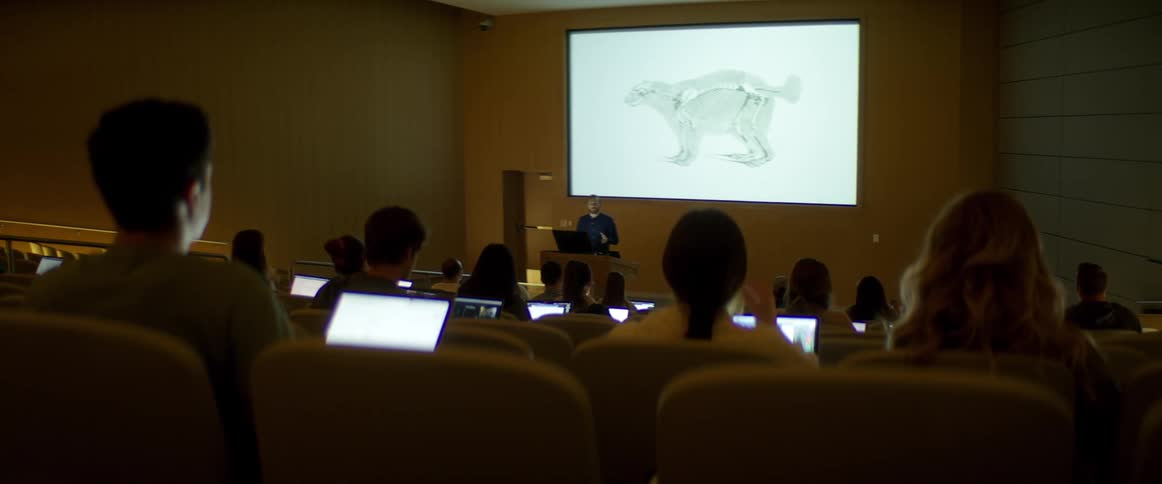 A professor stands in front of a class of students with laptops and gives a lecture