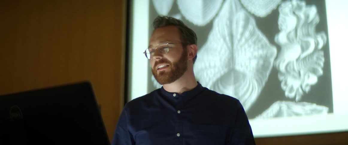 A man in front of a classroom smiling and talking