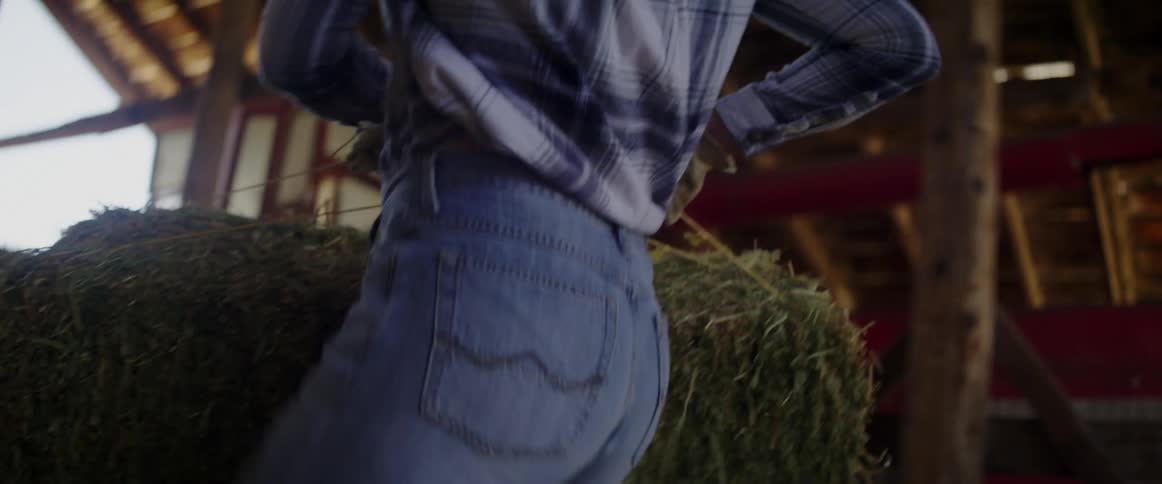 Woman work wearing jeans and gloves carry hay bales inside a barn