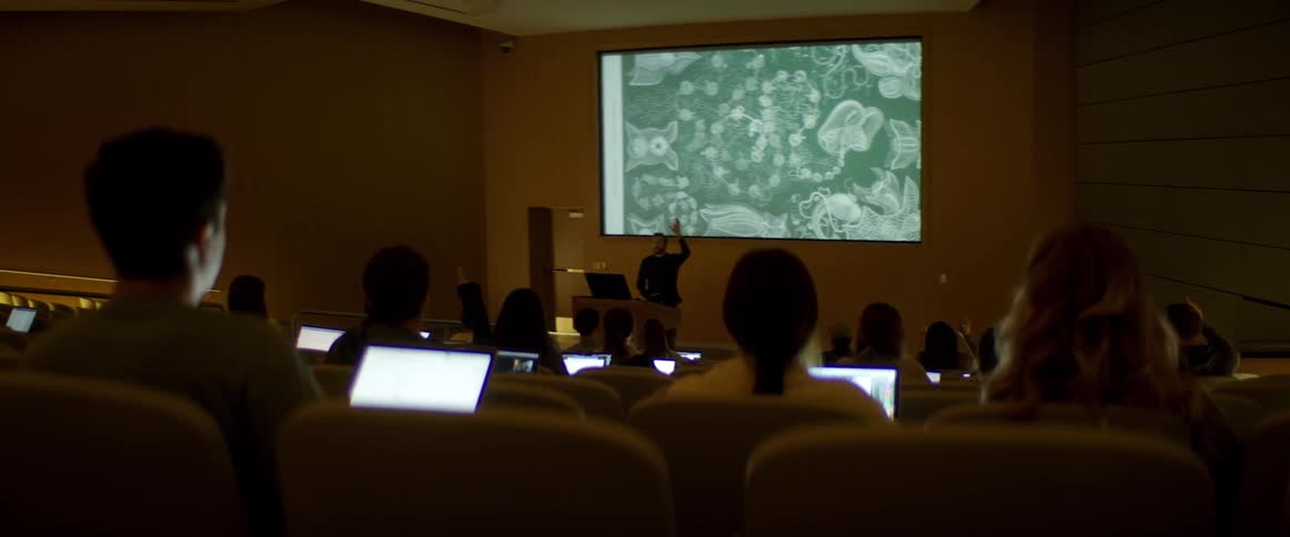People sitting in an auditorium listening to a man speak
