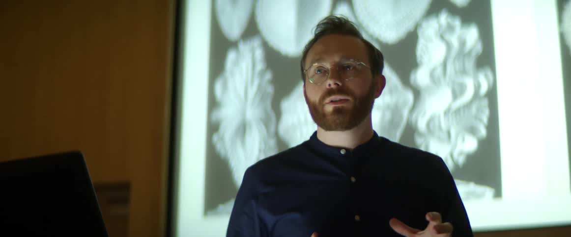 A teacher stands in front of a large screen and gives a lecture