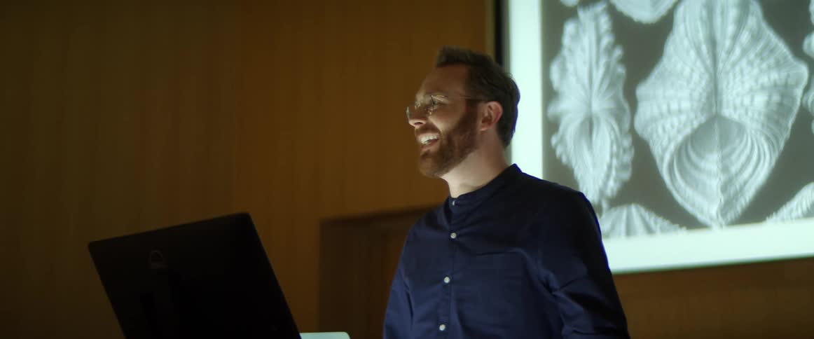 Man stands in front of a laptop as he speaks in an auditorium