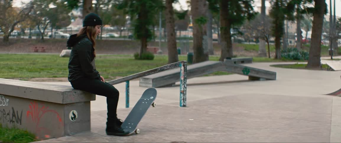 A girl sits on the wall with her skateboard in the park
