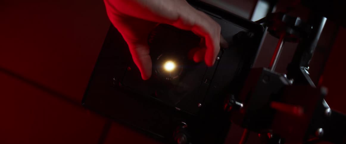 A white woman adjusts an aperture for a light bulb in a scientific device