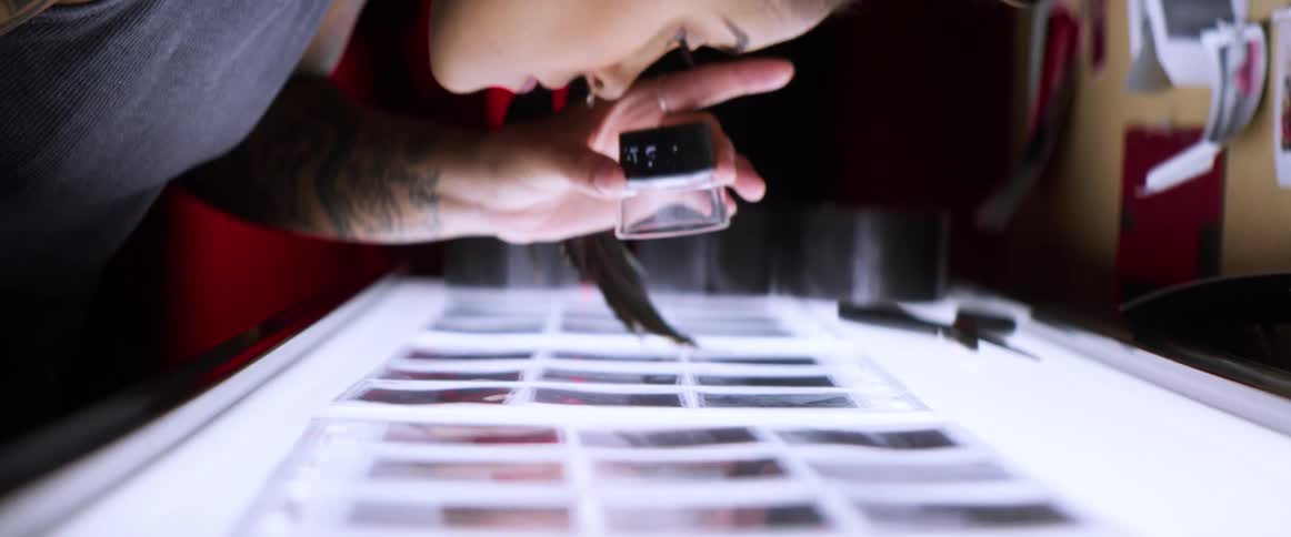 A woman uses a magnifying glass to look at photos placed on a lighted table