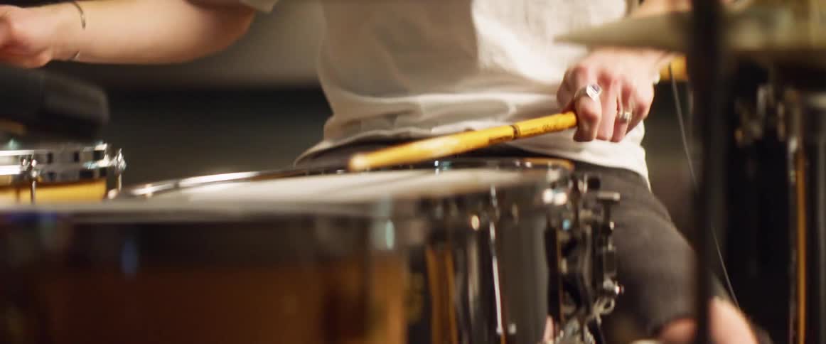 Male sitting on a stool bounces his leg as he plays the drums using drum sticks