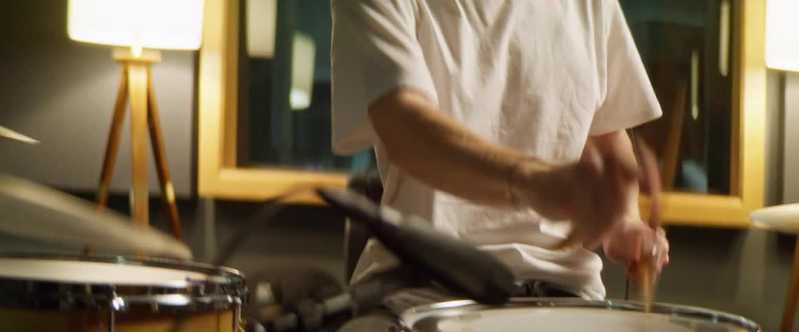 A man drumming in front of a mirror in a brightly lit room