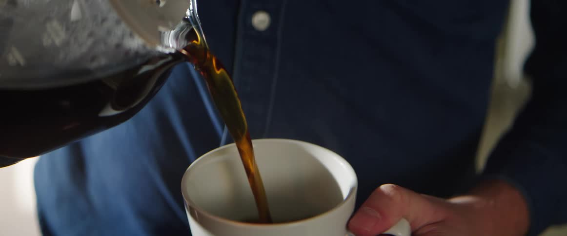 A person pours coffee from a coffee pot to a mug
