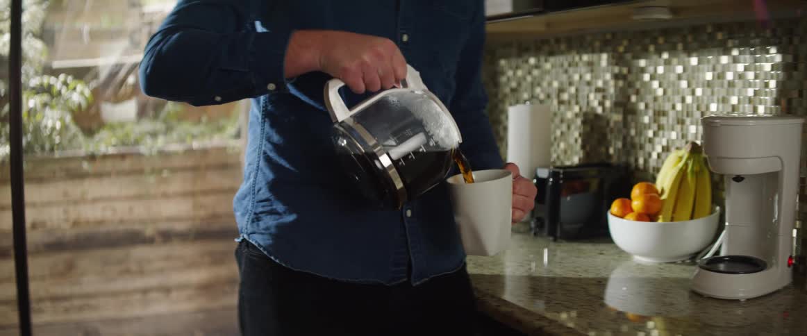 Man pours coffee from carafe into mug in kitchen