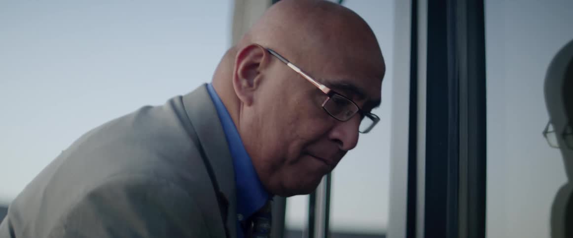 A man with a suit and glasses opening a door and entering a building