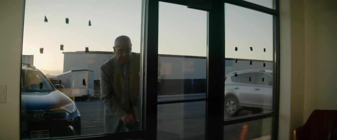 Male stands outside of business briefly before walking up and unlocking the glass door before entering the waiting area of the office