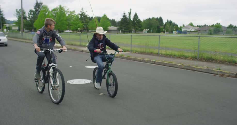 Two boys ride bicycles on a road on a cloudy day