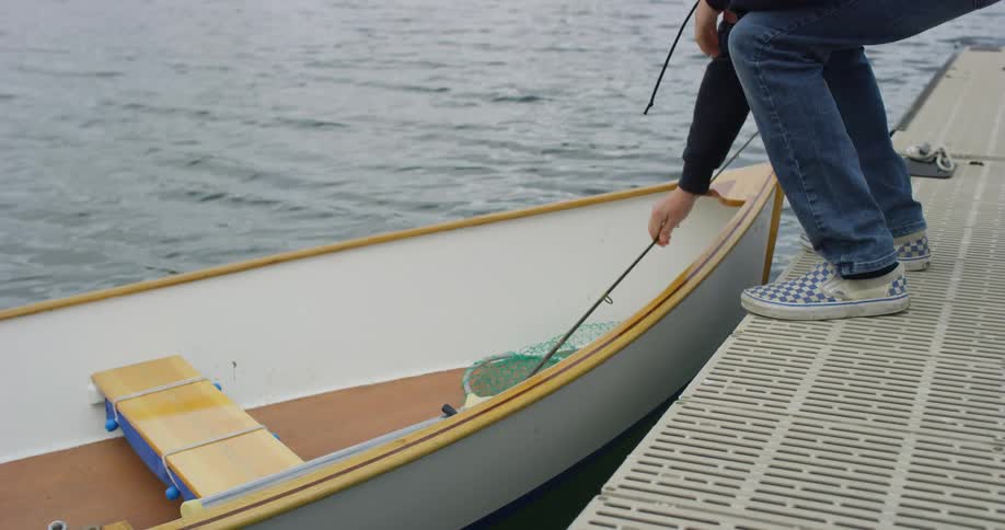 A person placing a fishing rod into a wooden boat