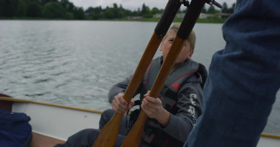 Father hands oars to son while in canoe on lake