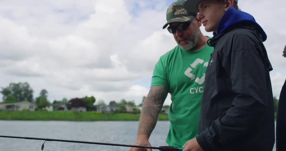 A father teaches his son how to fish in a lake near a neighborhood