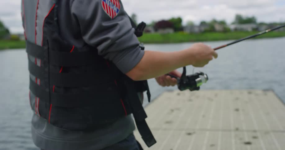 A man walks down a dock with a little fish on the end of his fishing pole