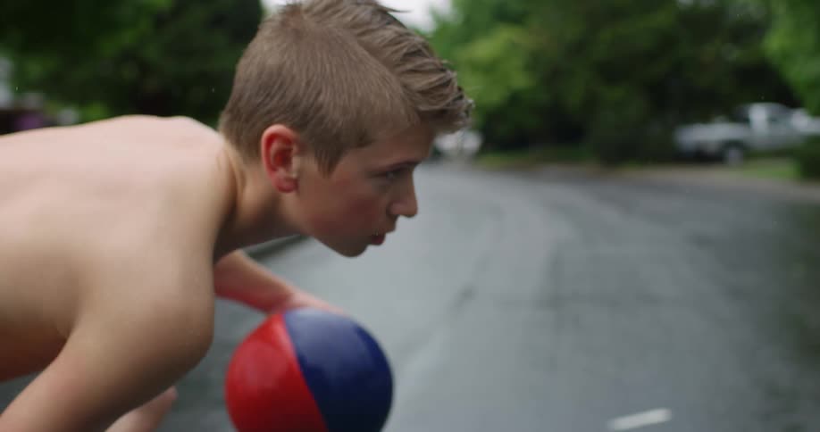 A boy is bouncing the basketball on the wet street
