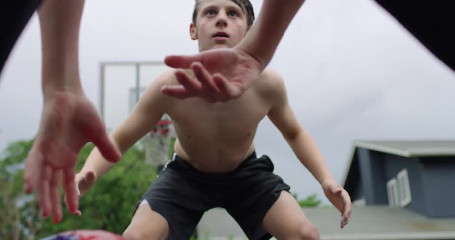 A shirtless boy carefully watching and guarding another boy to prevent him from scoring with the basketball