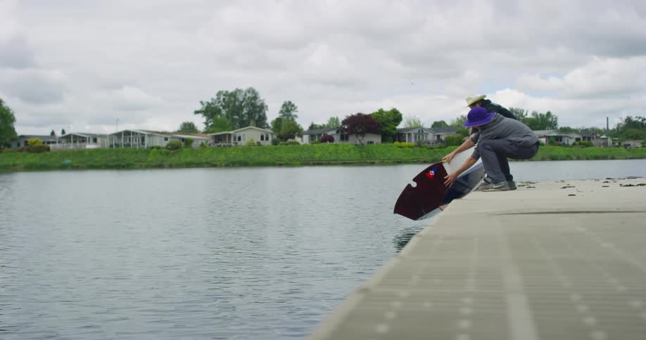 Two boys place small boat in water from dock on lake