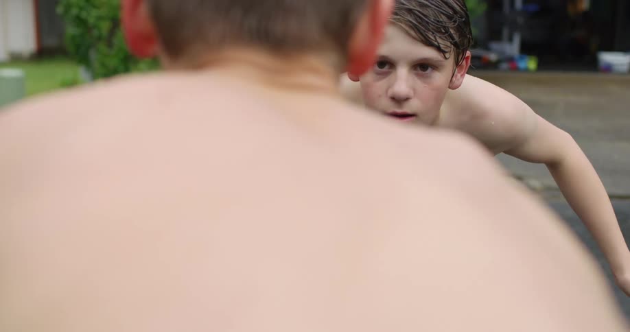 A pair of boys in swimming trunks face down each other in preparation for grappling
