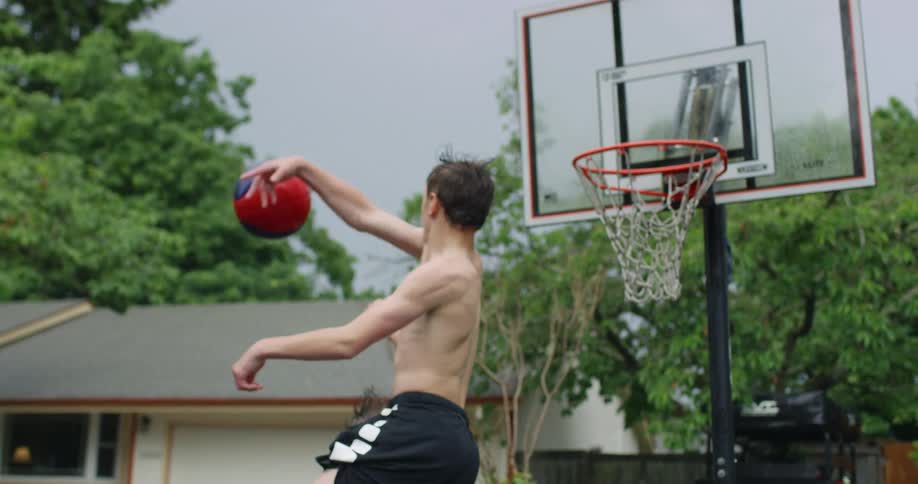 Two young men play basketball together near a home garage