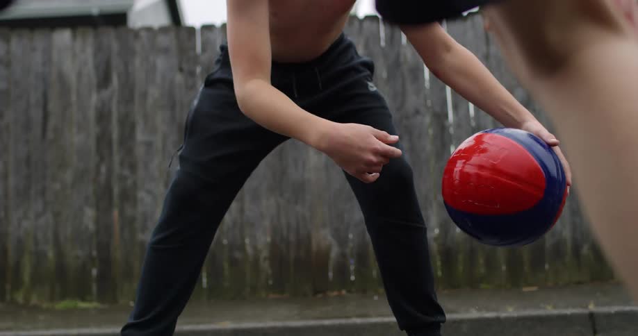 A white male bounces a basketball in the street in front of an opponent