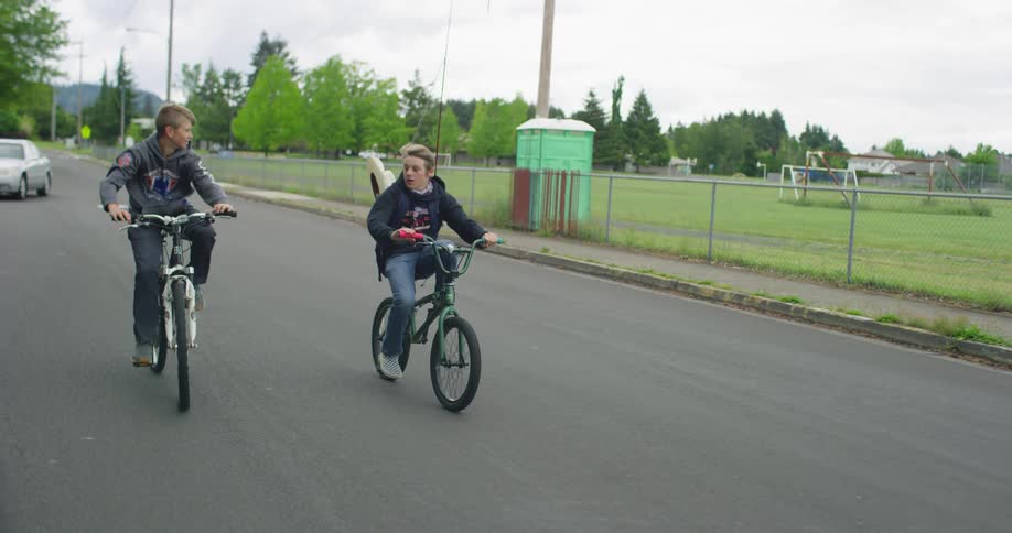 Two boys on bicycles with fishing rods riding on city street