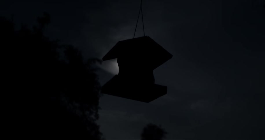 A birdhouse hangs from a wire outside at night