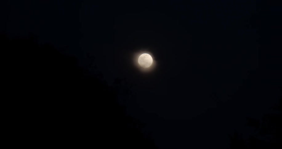 The moon glows behind slight haze in the night sky
