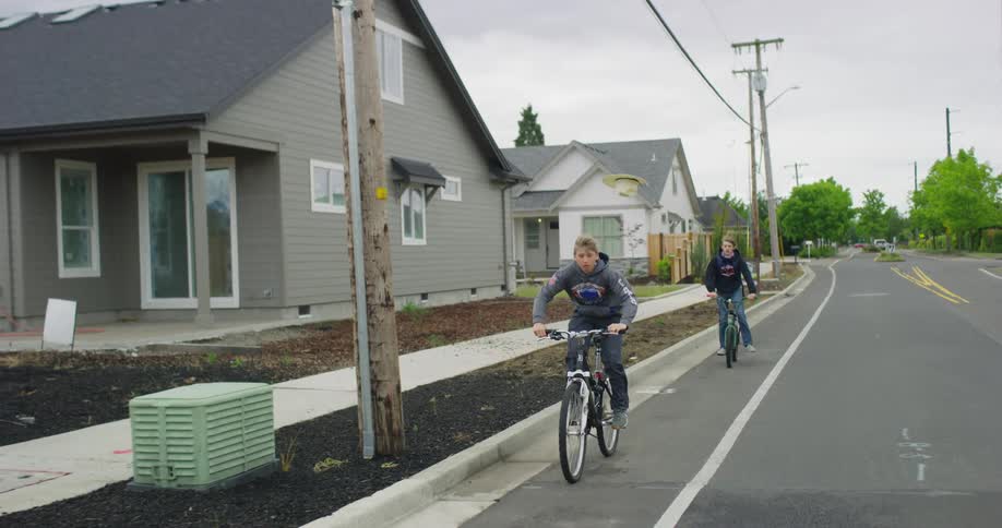Two teenage boys ride bicycles down a street